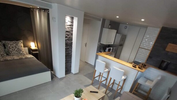 A modern living room with a sofa, a coffee table, and a dining area with chairs. There is a kitchen area with a microwave and cabinets. - Studio Villa Nui GH (Cuers)