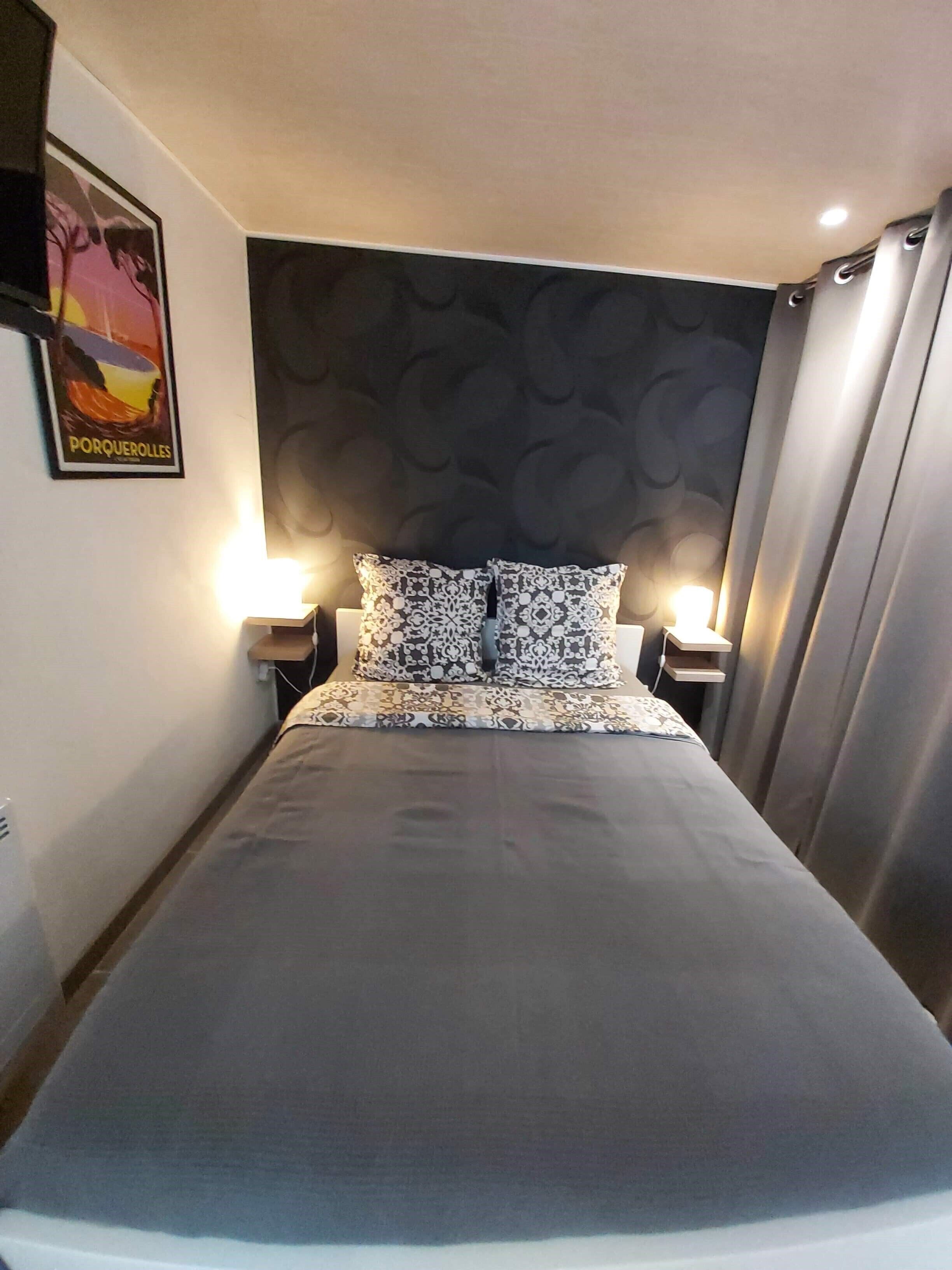 A hotel room with a large bed, two bedside tables with lamps, a patterned headboard, and a poster on the wall.
