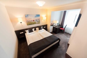A hotel room with a bed, bedside tables, a desk with a chair, a lamp, and a painting on the wall. - Double room - Hotel Villa Belvedere (Binz)