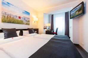 A hotel room with two beds, a desk, a chair, a TV, and a painting on the wall. - Double room - Hotel Villa Belvedere (Binz)