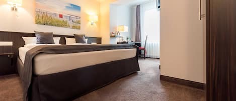 A hotel room with a large bed, bedside tables, a desk, a chair, a lamp, a painting on the wall, and a door.