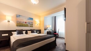 Ein Hotelzimmer mit einem großen Bett, Nachttischlampen, einem Schreibtisch, einem Sessel und einem Fernseher.