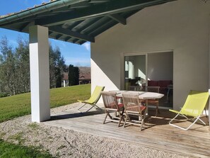 Eine überdachte Terrasse mit Tisch und Stühlen, eine Rasenfläche und im Hintergrund ein Haus.