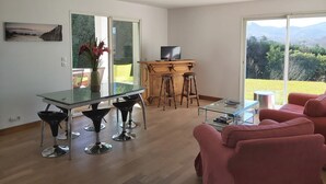 Uma sala de estar moderna com uma mesa de jantar de vidro, dois banquetes, um móvel de TV de madeira e um sofá vermelho.