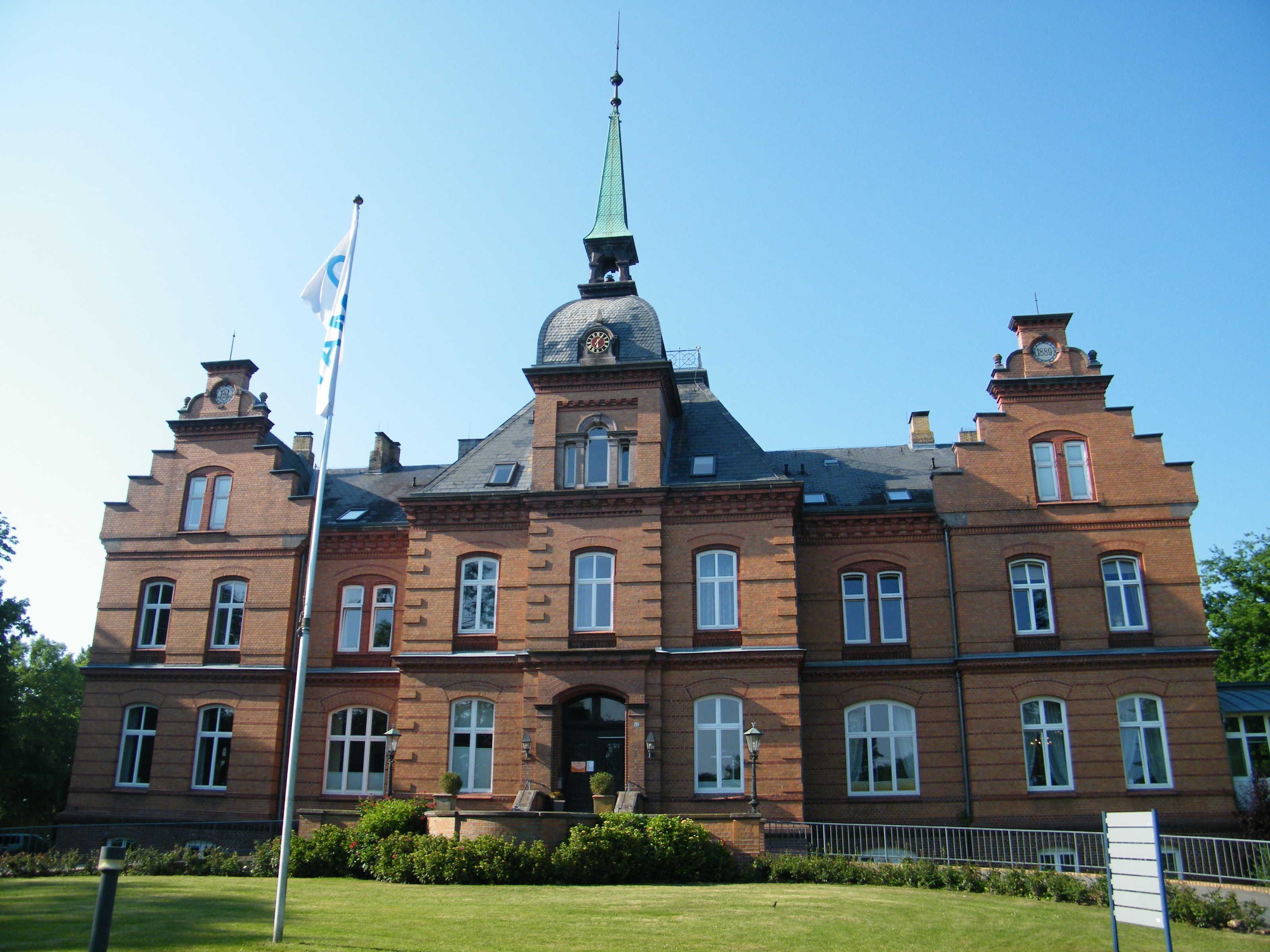 A large, historic building with a prominent clock tower, multiple windows, and a flagpole.