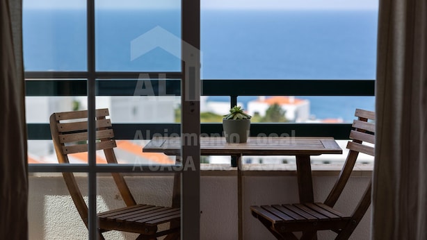 Un balcón con dos sillas de madera y una mesa, con vista al mar.