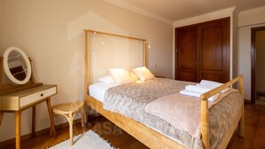 Un dormitorio con una cama de madera con dosel, un pequeño escritorio de madera con espejo y un taburete de mimbre.