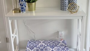 Ein weißer Konsolentisch mit einem gemusterten Kissen, einer Vase, einer Topfpflanze, einer Lampe und Dekorationselementen.