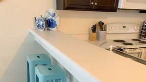 Eine Küche mit weißer Arbeitsplatte, vier hellblauen Hocker, einem Herd und einem Schrank über der Arbeitsfläche.