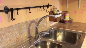 A kitchen with a stainless steel sink, a black metal rack with hooks, and a tiled backsplash. - B&B Casa Mucci (Sestola)