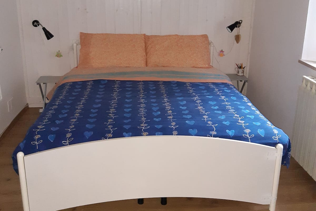 A bed with a blue patterned bedspread, two pillows, and two wall-mounted lamps.