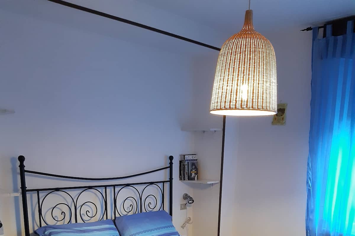 A bed with a metal frame, a blue and red bedspread, and a hanging light fixture.
