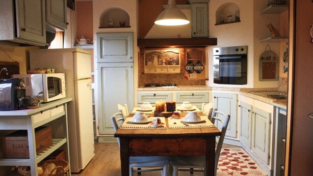A compact kitchen with white cabinets, a dining table set for four, and a vintage microwave. - B&B Casa Mucci (Sestola)