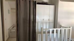 Ein Zimmer mit einem weißen Kleiderschrank, einem weißen Babybett und einem grauen Vorhang.