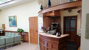 Un vaste espace de vie comprenant un bar en bois aux lignes courbes, un canapé vert et une machine à café.