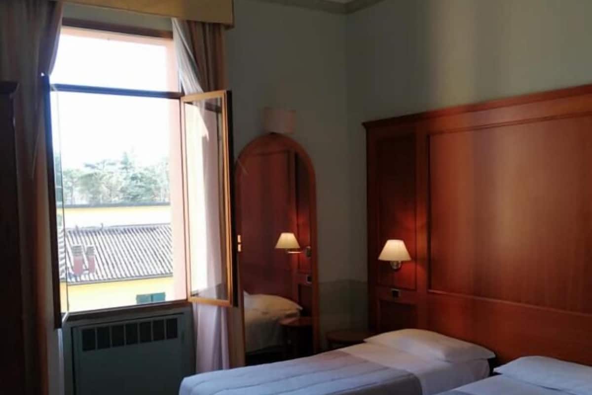 Ein Hotelzimmer mit zwei Betten, einem Schreibtisch, einem Stuhl und einem Fenster mit Vorhängen.