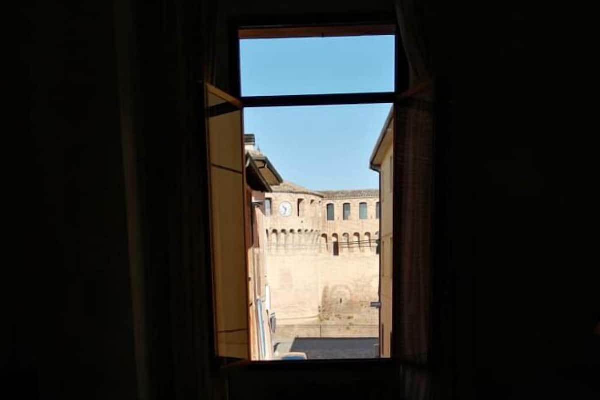 Ein schwach beleuchteter Raum mit einem Bett und einem Fenster mit Blick auf ein Gebäude mit Bögen.