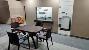A dining area with a table and chairs, a refrigerator, and a tiled backsplash. - Sukhmani Homestays. Your own space in a private bungalow. (KOLKATA)