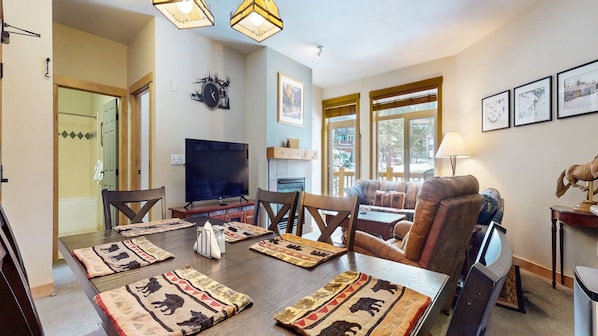 A spacious living room with a large dining table, comfortable seating, a flat-screen TV, and a fireplace.