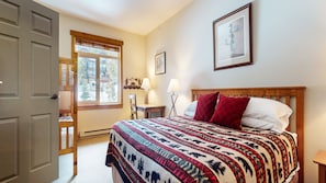 A bedroom with a bed, a window, a door, and a nightstand.