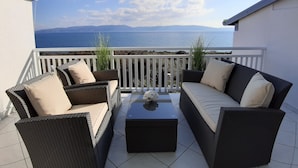 Un balcone con mobili in vimini, un tavolino e vista mare e montagne.