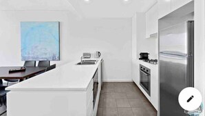 Een moderne keuken met witte kasten, een roestvrijstalen koelkast en een eethoek met een tafel en stoelen.