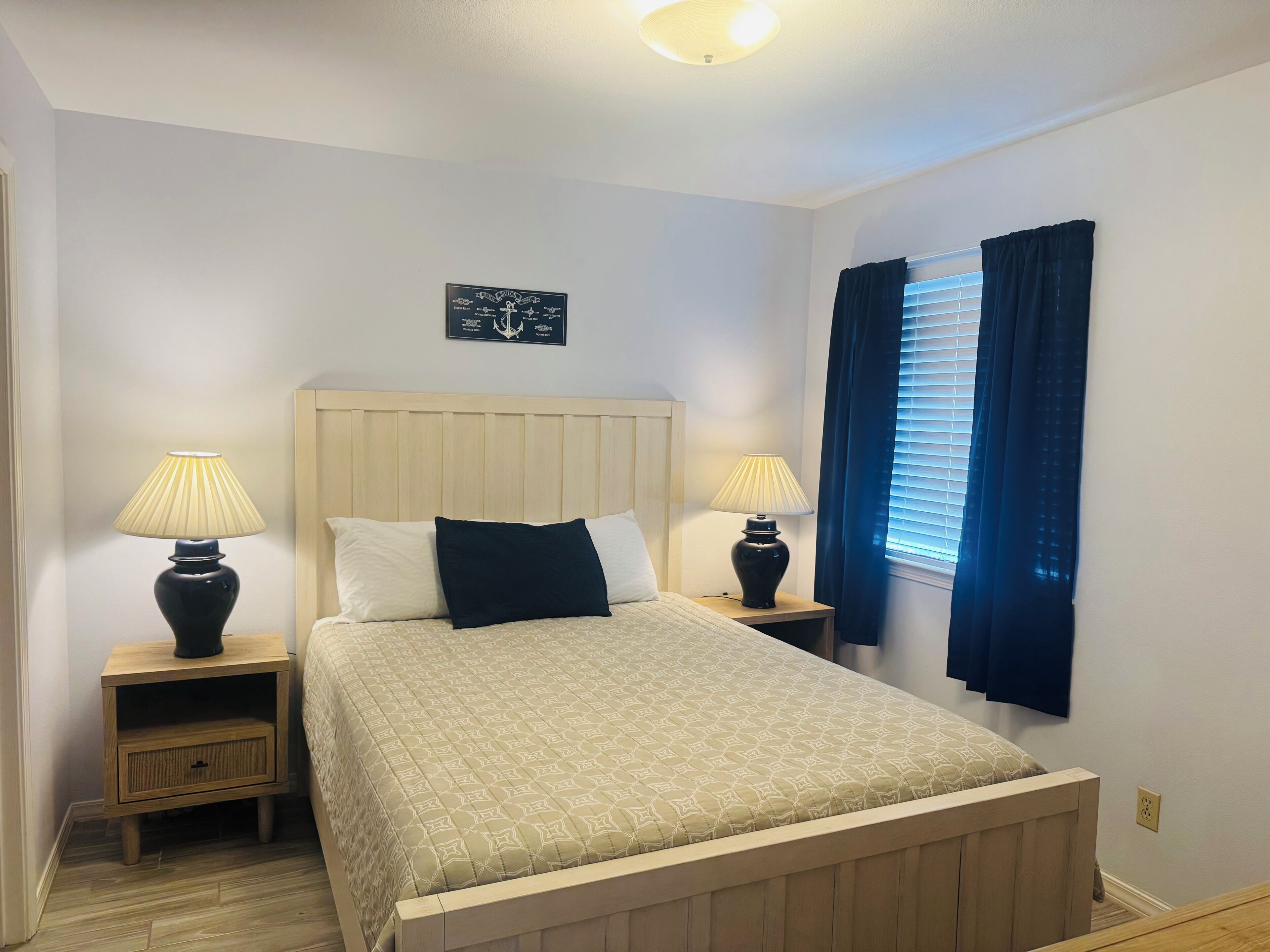 A neatly arranged bedroom with a bed, two bedside tables with lamps, a wall-mounted artwork, and a window with curtains.