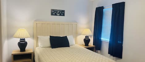 A neatly arranged bedroom with a bed, two bedside tables with lamps, a wall-mounted artwork, and a window with curtains.