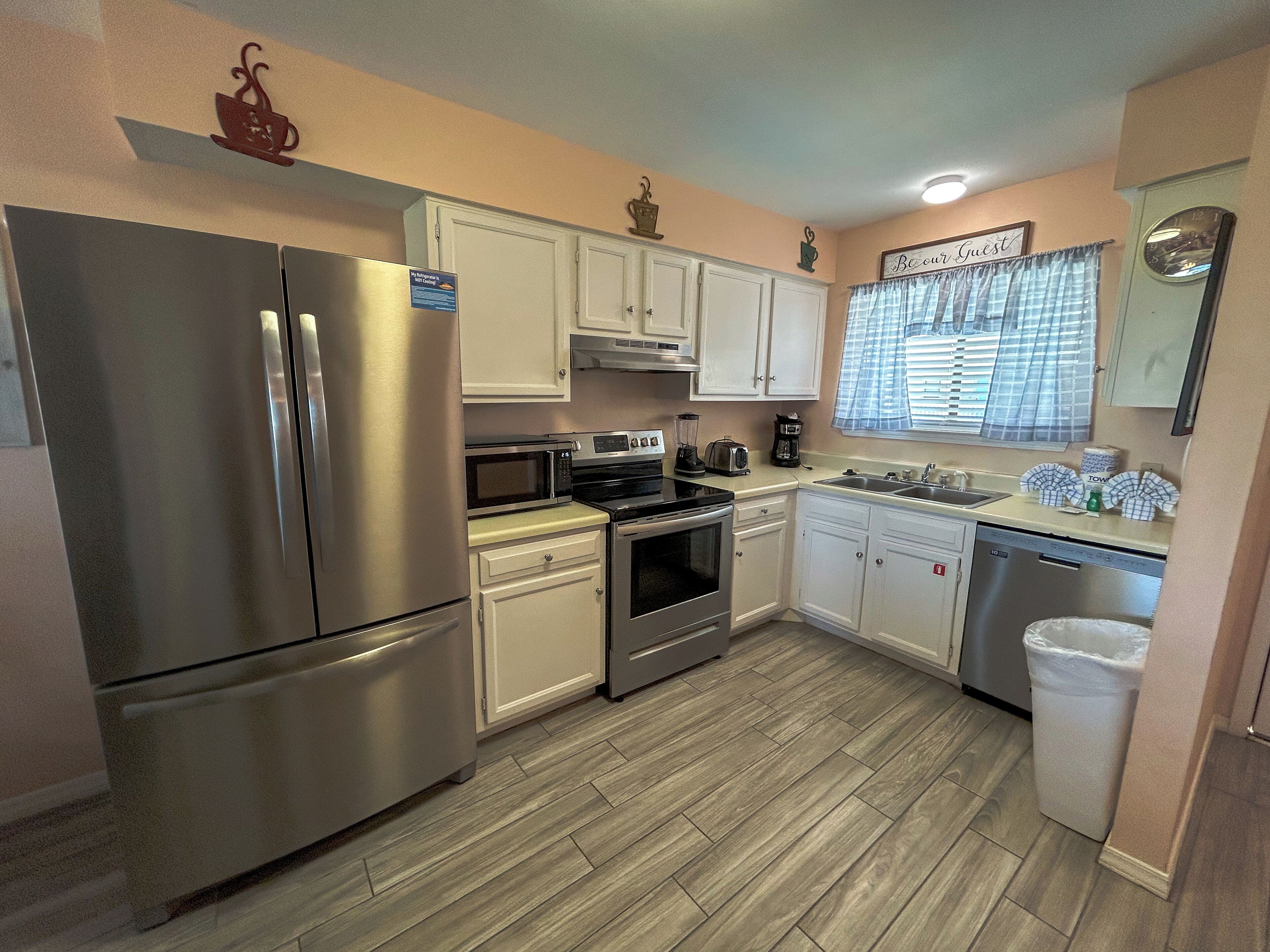 A modern kitchen with stainless steel appliances, white cabinets, and a wooden floor.