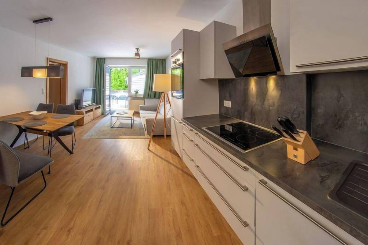 Une cuisine moderne dotée d’une grande cuisinière, d’un coin repas avec une table et des chaises en bois, et offrant une vue sur l’extérieur grâce à une porte vitrée.