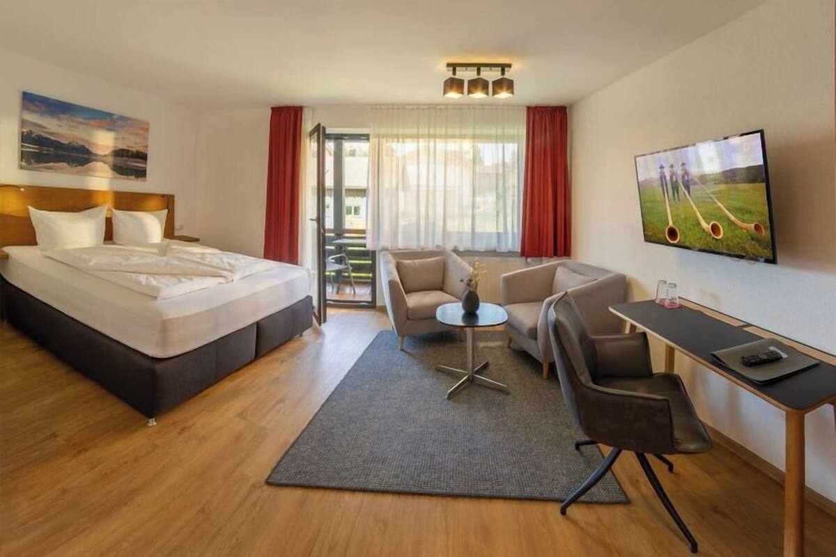 Une chambre d’hôtel avec un lit, un bureau, deux chaises, une petite table et un téléviseur.