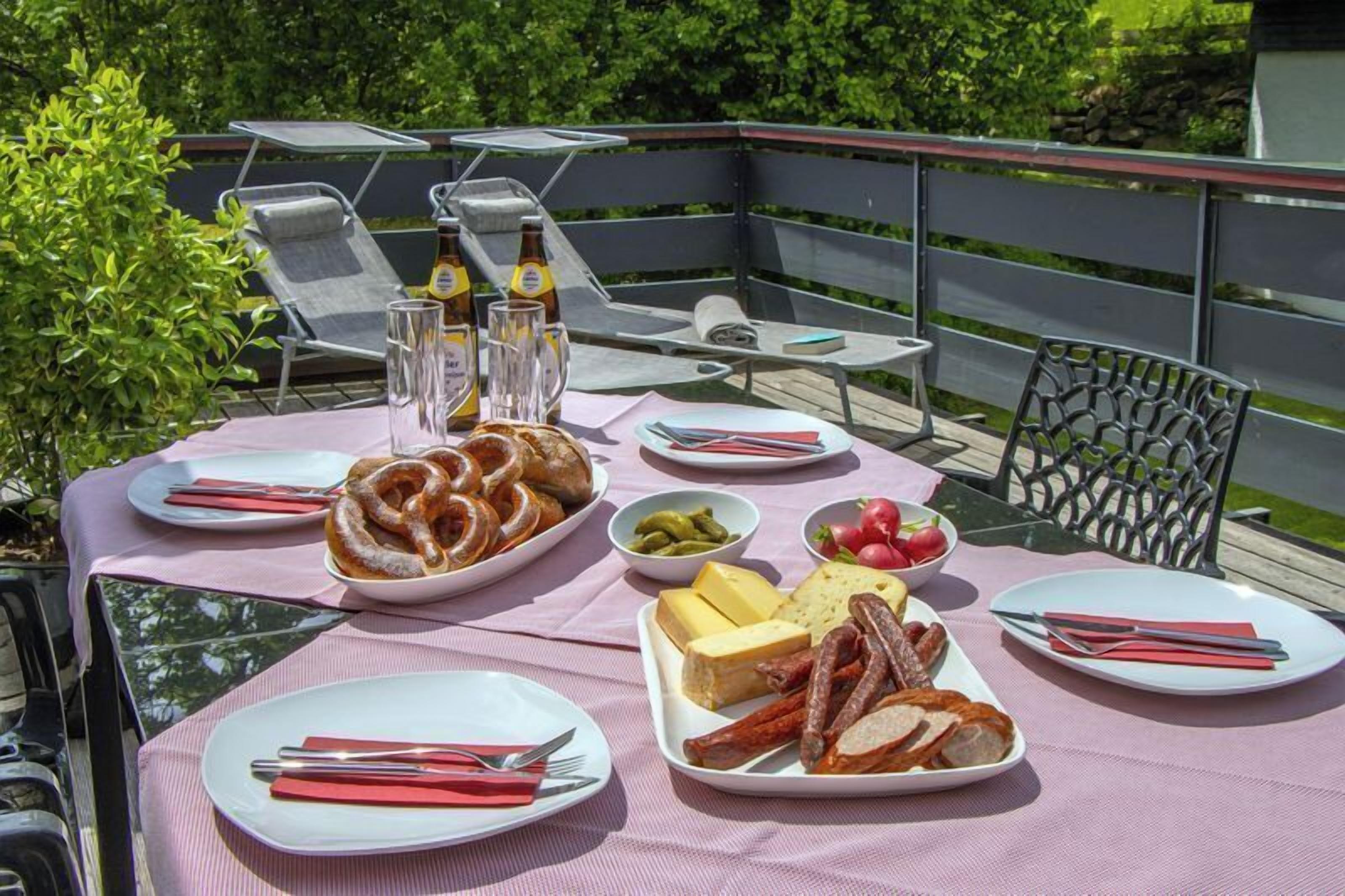 Ein Essbereich im Freien mit einem Tisch, der für eine Mahlzeit gedeckt ist, darunter Teller mit Speisen, Besteck und eine Bierflasche.