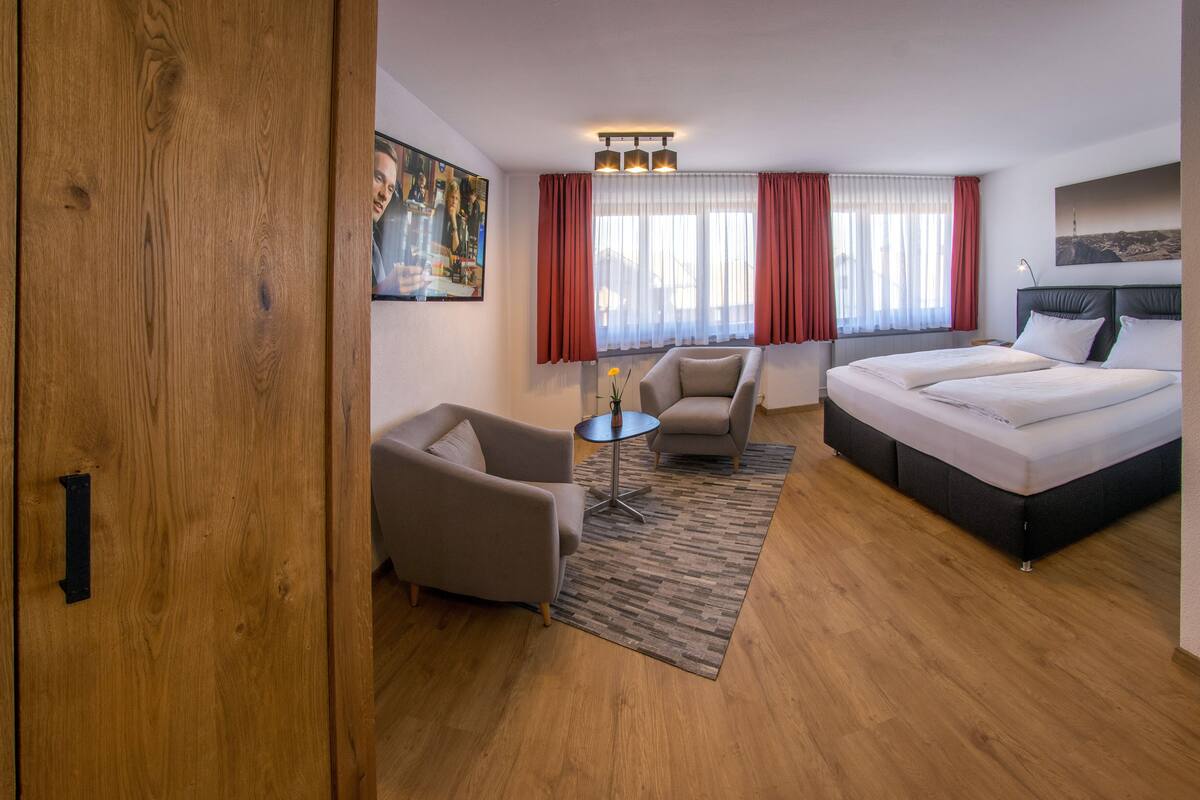 Une chambre d’hôtel avec un lit, deux fauteuils, une petite table et un tapis.