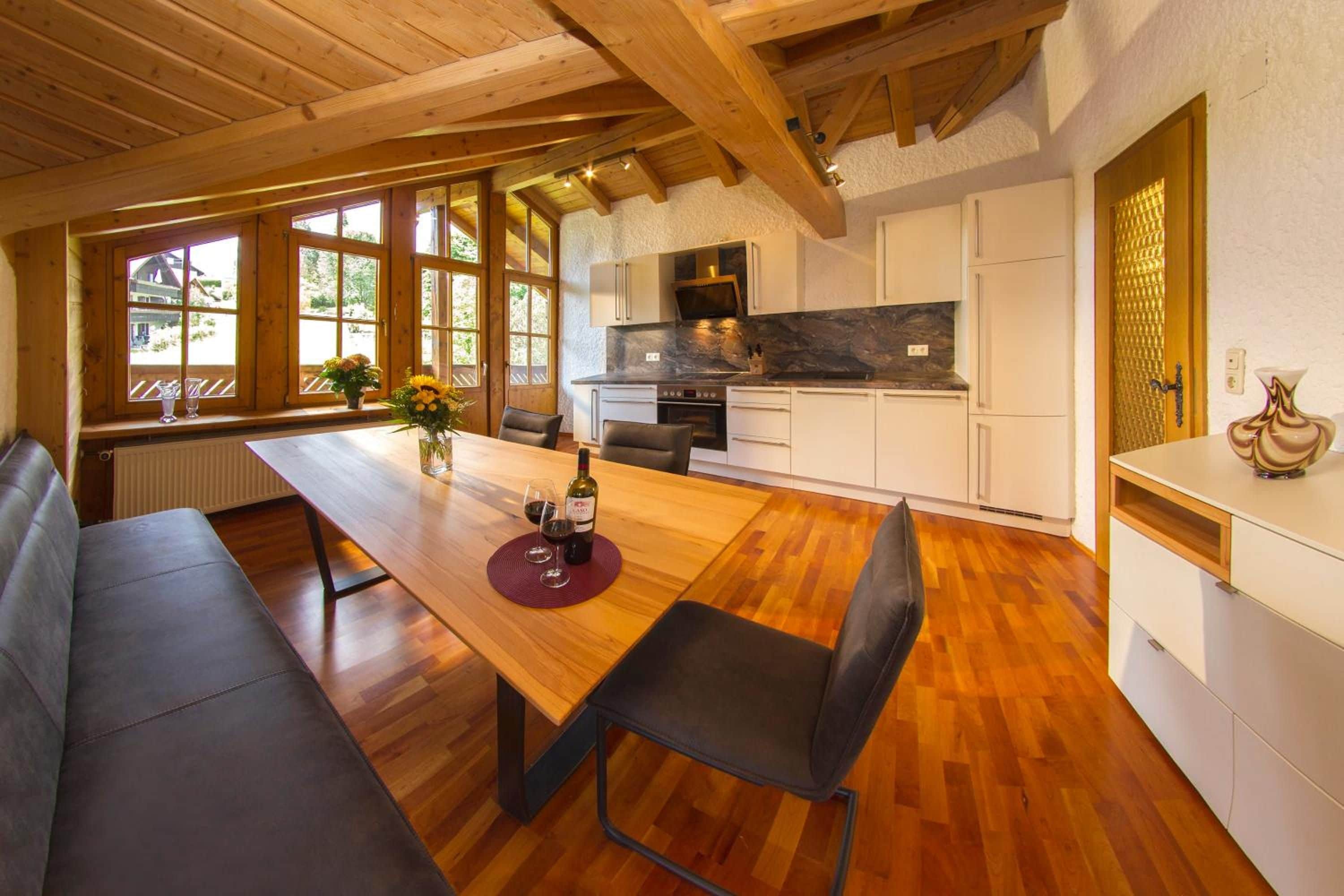 Eine moderne Küche mit weißen Schränken, einer Marmorarbeitsplatte und einem Holztisch mit zwei Stühlen.