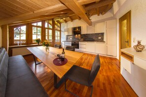 Een moderne keuken met witte kastjes, een marmeren aanrecht en een houten eettafel met twee stoelen.