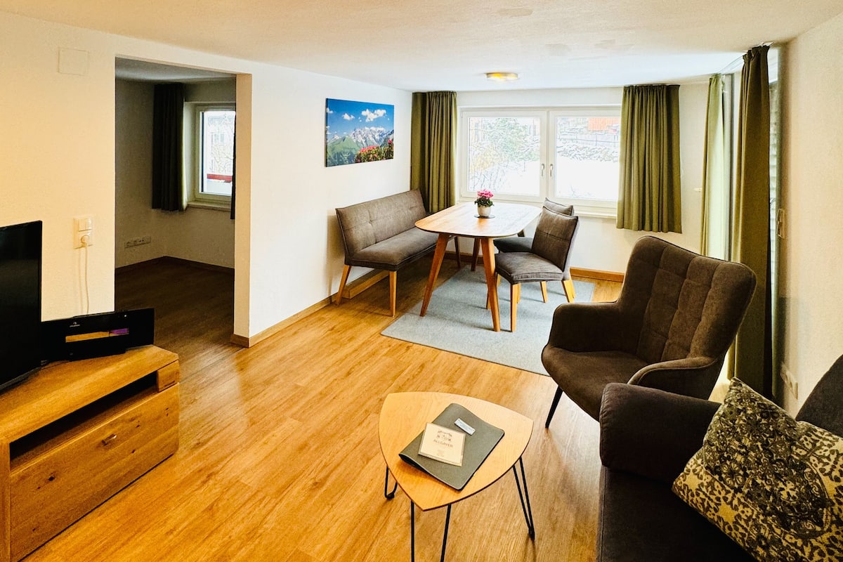 Un salon moderne avec un plancher en bois, un canapé, une table à manger avec des chaises, un meuble pour la télévision et un tableau accroché au mur.