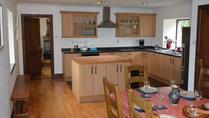 Een keuken met houten kasten, een centraal kookeiland en een eettafel voor vier personen.