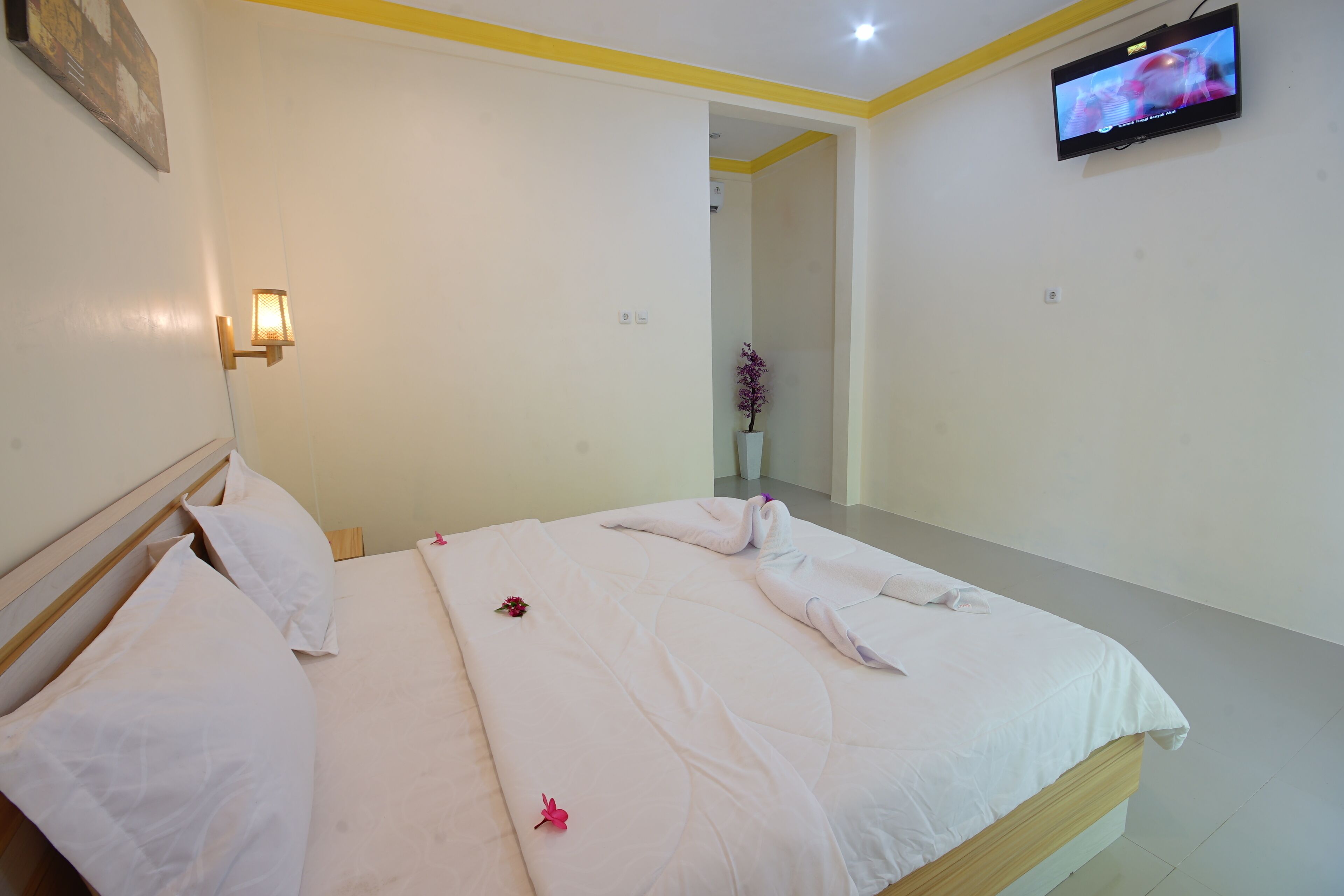 A hotel room with a bed, pillows, a wall-mounted TV, and a small potted plant.