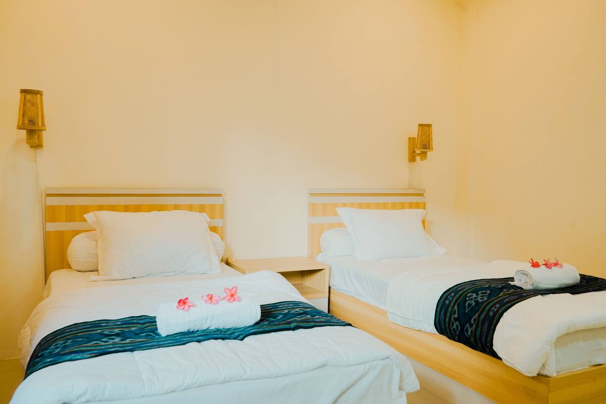Une chambre d’hôtel avec deux lits simples, chacun doté d’une tête de lit en bois, de draps blancs et d’une petite table de chevet.