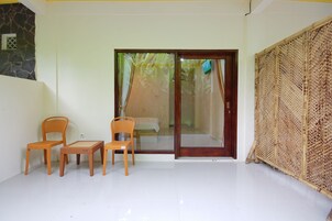 Quarto com porta de vidro deslizante para uma varanda, duas cadeiras de madeira e uma pequena mesa.