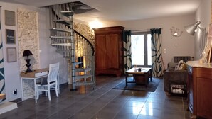 Un vaste espace de vie agrémenté d’un mur en pierre, d’un escalier en bois, d’une cheminée et d’un coin repas avec une table et des chaises.