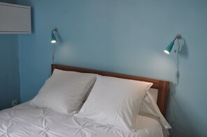 Un lit avec une literie blanche et deux lampes fixées au mur.