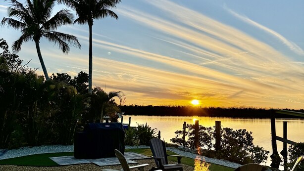 A serene lakeside patio with outdoor seating and a fire pit, overlooking a sunset. - Matlacha Sunset Cottage (Matlacha)