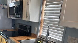 A modern kitchen with stainless steel appliances, wooden countertops, and a window with blinds. - Matlacha Sunset Cottage (Matlacha)