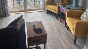 A living room with a view of a lake, a table with a remote control, and a lamp on a side table. - Matlacha Sunset Cottage (Matlacha)