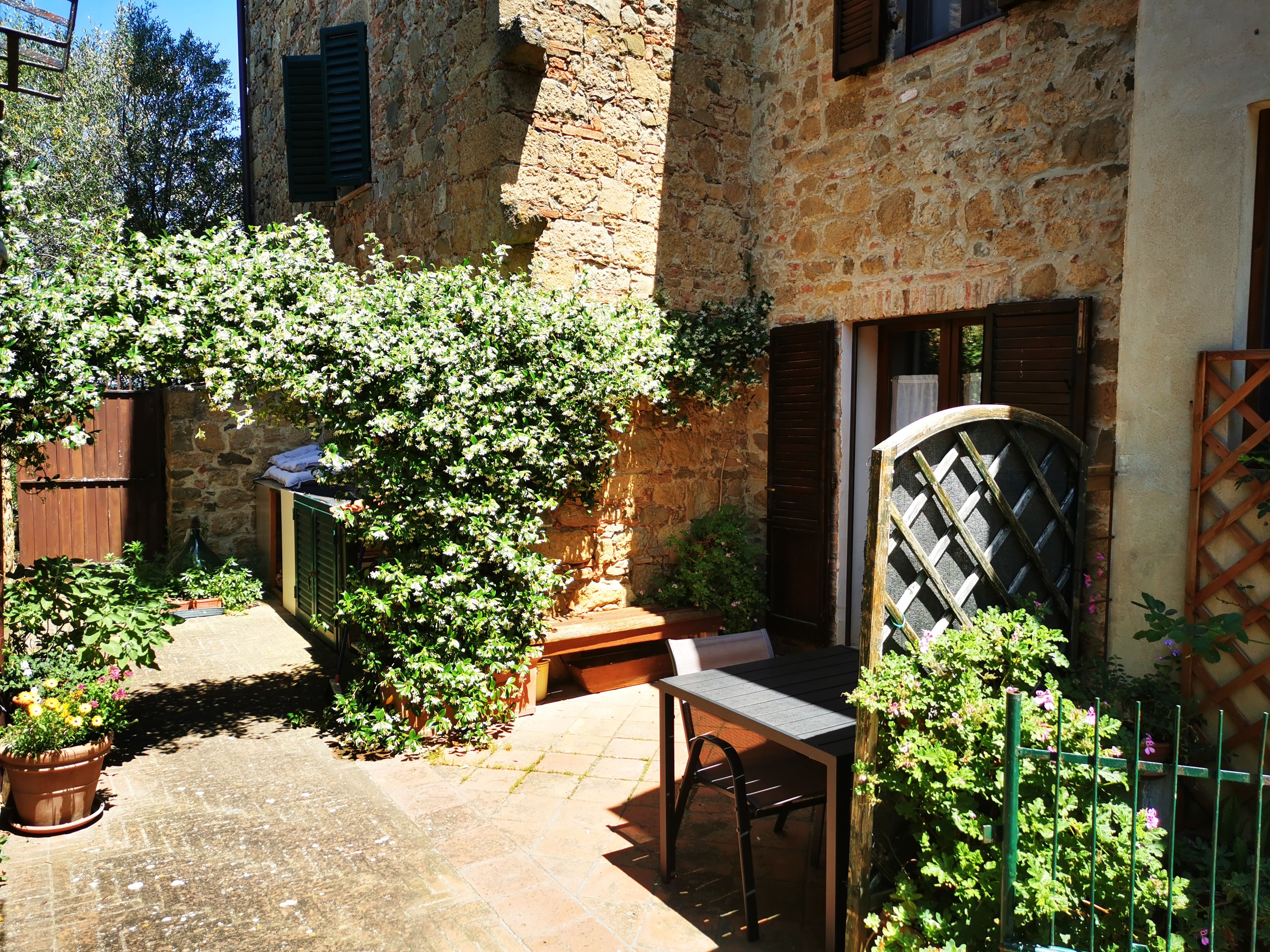 A stone building with a wooden door, a table with a chair, and potted plants.