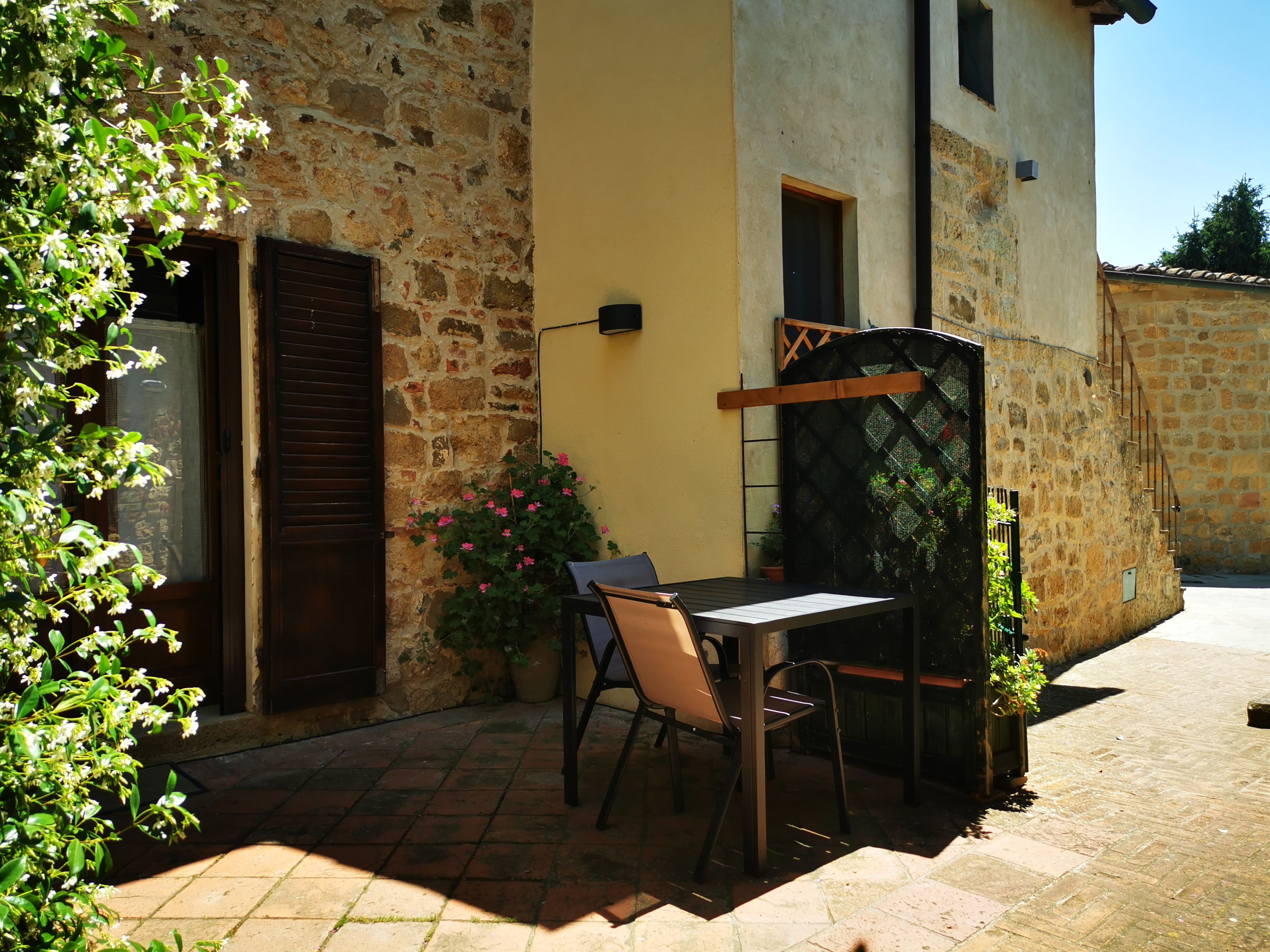 An outdoor patio with a table and chairs, a stone wall, and a wooden door.