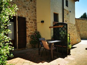 Un patio al aire libre con una mesa, sillas, un muro de piedra y una puerta de madera.