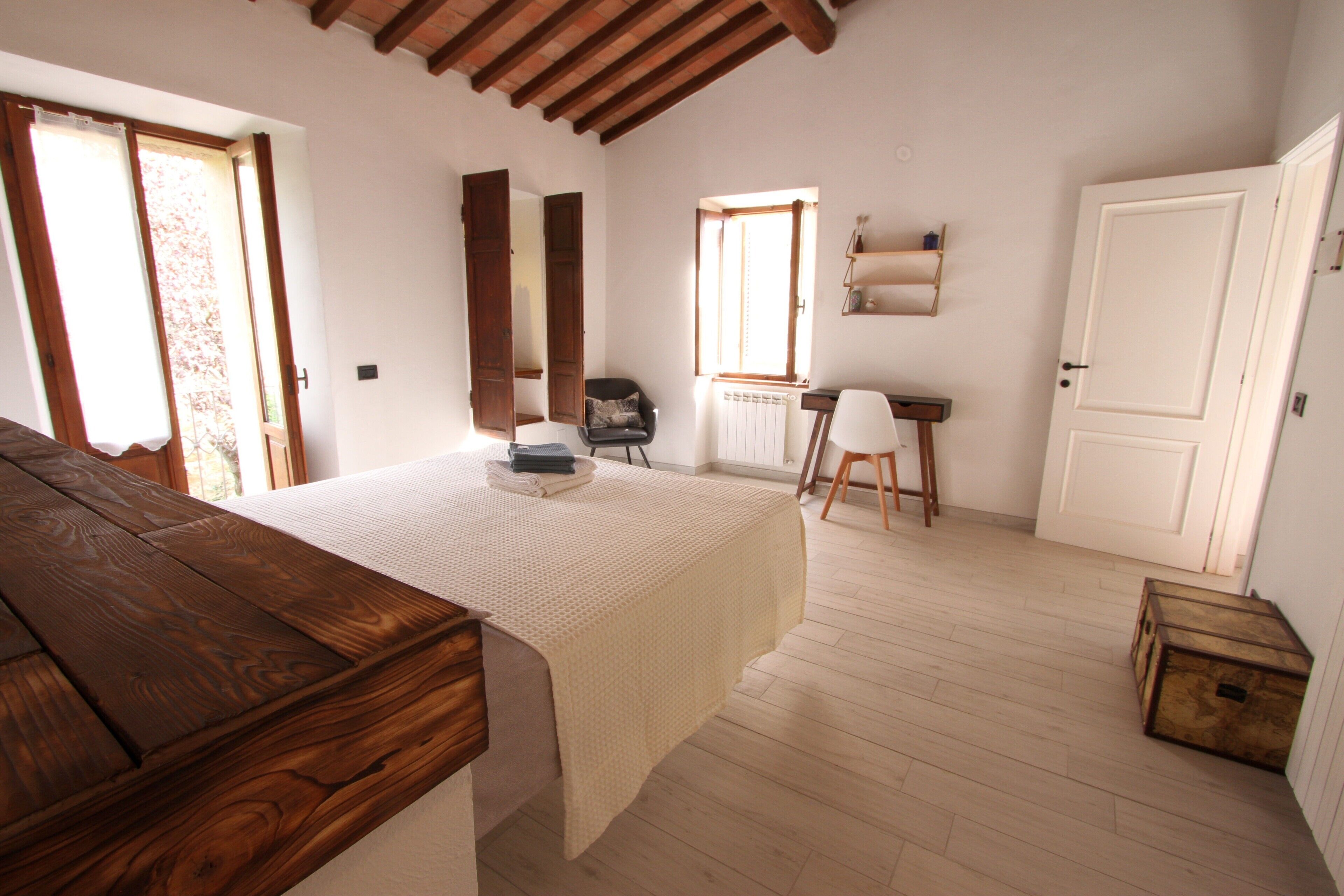 Un dormitorio con cama de madera, un escritorio y una silla. Hay un radiador y una ventana con cortinas.
