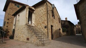 A stone building with a staircase leading to a door, a small balcony, and a street in front.